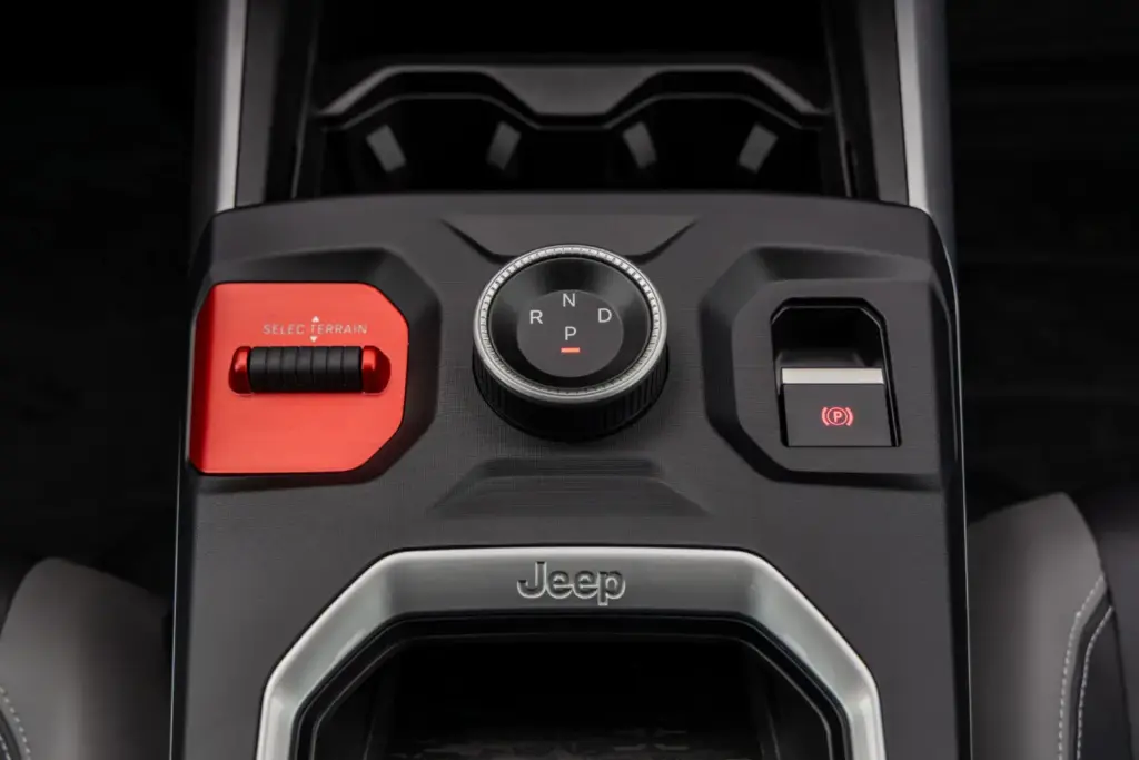 La tercera generación del Jeep Compass llega con una perspectiva global, fusionando el diseño icónico de la marca con un elevado nivel de equipamiento y una amplia dotación tecnológica pero, sobre todo, con una calidad de rodadura adaptada a los estándares europeos y, por qué no decirlo, con una puesta a punto perfecta para nuestras hoy maltrechas carreteras. Lo primero que llama la atención es que este Jeep Compass –que hemos probado en su versión eléctrica de lanzamiento– es claramente más grande que su predecesor y muestra un aspecto rotundo y cúbico que ha obligado a trabajar cada centímetro cuadrado de la carrocería para lograr un coeficiente aerodinámico de 0,29, meritorio para unos volúmenes tan poliédricos. El Jeep Compass se desmarca de sus “mellizos” de Stellantis Con 4,55 metros de longitud, Jeep lo define como SUV del segmento C, aunque sus dimensiones lo acercan claramente al segmento superior. Basado en la plataforma modular STLA Medium de Stellantis –compartida con los Peugeot 3008 y 5008, el Opel Grandland y el Citroën C5 Aircross–, el Jeep Compass se beneficia de un desarrollo de suspensiones específico orientado a lograr 20 centímetros de altura libre al suelo, con una reducción del 15 % en la aceleración vertical y un 20 % menos de balanceo de carrocería respecto a la generación anterior. El resultado sobre el asfalto es el de un buen SUV: no especialmente ágil, como corresponde a su masa y a su centro de gravedad elevado, pero sí notablemente mejor que el anterior Jeep Compass. Se inclina moderadamente en los apoyos fuertes y en las frenadas enérgicas, pero sin el efecto rebote de las suspensiones que caracterizaba a la generación precedente, poniendo en valor el trabajo de unos amortiguadores perfectamente capaces de cumplir con su trabajo. Las suspensiones están, así, bien adaptadas para recorrer caminos a buen ritmo: absorben con solvencia las irregularidades del terreno y muestran una parte final del recorrido más firme para evitar topes si se aborda una zona abrupta a más velocidad de la debida. En los caminos moderadamente rotos, el Compass pone en valor sus amplios recorridos de suspensión y la amabilidad con la que trata a sus ocupantes, y en autopista cumple con eficacia. En unos tiempos en los que nuestras carreteras acumulan socavones y baches por la falta de mantenimiento y el paso de las últimas borrascas, un vehículo como este Jeep Compass resulta más interesante de lo que parece. La dirección, además, ofrece un tacto suave, muy asistido, que minimizará el efecto “latigazo” ante un bache imprevisto, y el radio de giro es razonable para la batalla del vehículo. Al volante del Jeep Compass eléctrico, el motor de 213 CV ofrece la respuesta inmediata que cabe esperar de esta tecnología, pero con una progresión suave y lineal que casa bien con el carácter del vehículo. La frenada regenerativa está bien integrada, y el modo One Pedal –que detiene el vehículo por completo– es muy práctico, aunque resulta algo llamativo que se active mediante un botón dedicado en lugar de mediante las levas, como los otros tres niveles de regeneración. En cuanto a la autonomía homologada de 500 km WLTP, conviene aplicar el habitual factor corrector del 0,7 para hacerse una idea realista del alcance en uso cotidiano. Salto de calidad a bordo del nuevo Jeep Compass Por calidad de acabados y espacio, el habitáculo no tiene nada que ver con lo visto hasta ahora en el Jeep Compass. El puesto de conducción es cómodo, con una postura elevada muy Jeep, y las plazas traseras son amplias y adecuadas para el uso diario. El maletero ofrece 550 litros –45 más que en el anterior Jeep Compass–, ampliables con el gran hueco bajo el piso desmontable, aunque no hay maletero delantero. Un detalle relevante: el selector del cambio es un mando giratorio físico e intuitivo, en lugar del habitual conmutador lineal del resto de modelos de Stellantis, uno de los muchos detalles que indican que en Jeep se han tomado muy en serio este desarrollo y no han ido simplemente a “recarrozar” lo ya existente. El sistema Selec-Terrain ofrece cinco modos –Automático, Deportivo, Nieve, Arena/Barro y Eléctrico–, y hemos comprobado que el modo Arena permite un cierto patinamiento de las ruedas, lo que denota una buena calibración del control de tracción para ese tipo de terreno, incluso en un vehículo de tracción delantera. La insonorización es notable, por encima de la media de su segmento. La gama de lanzamiento incluye dos acabados: Altitude y First Edition. No es, con ninguno de ellos, un SUV que pretenda competir en precio, pero puede ser la opción adecuada para quienes necesiten capacidades fuera del asfalto superiores a las habituales en un 4x2. Quienes precisen un 4x4 real deberán esperar a la versión eléctrica bimotor, pero para las bacheadas carreteras de las que disfrutamos estos días, esta versión es más que suficiente. El Jeep Compass milita en el segmento más poblado del mercado, por lo que su fabricante ha decidido no competir en precio, sino ofrecer un producto que destaque por habitabilidad y bastidor. Su versión eléctrica añade economía de uso y etiqueta Cero. Así que estamos ante un modelo con argumentos para hacerlo bien, si bien su precio limitará su difusión.