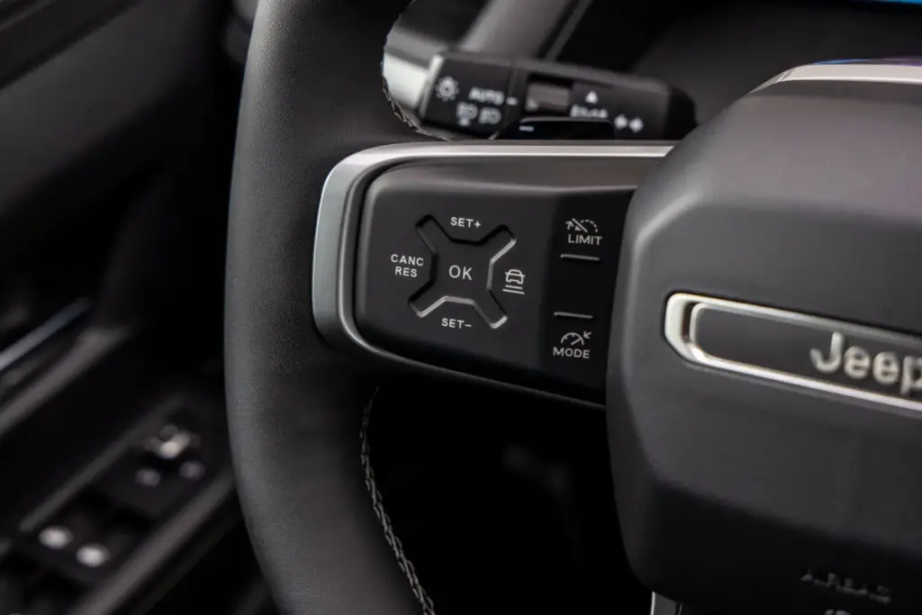 La tercera generación del Jeep Compass llega con una perspectiva global, fusionando el diseño icónico de la marca con un elevado nivel de equipamiento y una amplia dotación tecnológica pero, sobre todo, con una calidad de rodadura adaptada a los estándares europeos y, por qué no decirlo, con una puesta a punto perfecta para nuestras hoy maltrechas carreteras. Lo primero que llama la atención es que este Jeep Compass –que hemos probado en su versión eléctrica de lanzamiento– es claramente más grande que su predecesor y muestra un aspecto rotundo y cúbico que ha obligado a trabajar cada centímetro cuadrado de la carrocería para lograr un coeficiente aerodinámico de 0,29, meritorio para unos volúmenes tan poliédricos. El Jeep Compass se desmarca de sus “mellizos” de Stellantis Con 4,55 metros de longitud, Jeep lo define como SUV del segmento C, aunque sus dimensiones lo acercan claramente al segmento superior. Basado en la plataforma modular STLA Medium de Stellantis –compartida con los Peugeot 3008 y 5008, el Opel Grandland y el Citroën C5 Aircross–, el Jeep Compass se beneficia de un desarrollo de suspensiones específico orientado a lograr 20 centímetros de altura libre al suelo, con una reducción del 15 % en la aceleración vertical y un 20 % menos de balanceo de carrocería respecto a la generación anterior. El resultado sobre el asfalto es el de un buen SUV: no especialmente ágil, como corresponde a su masa y a su centro de gravedad elevado, pero sí notablemente mejor que el anterior Jeep Compass. Se inclina moderadamente en los apoyos fuertes y en las frenadas enérgicas, pero sin el efecto rebote de las suspensiones que caracterizaba a la generación precedente, poniendo en valor el trabajo de unos amortiguadores perfectamente capaces de cumplir con su trabajo. Las suspensiones están, así, bien adaptadas para recorrer caminos a buen ritmo: absorben con solvencia las irregularidades del terreno y muestran una parte final del recorrido más firme para evitar topes si se aborda una zona abrupta a más velocidad de la debida. En los caminos moderadamente rotos, el Compass pone en valor sus amplios recorridos de suspensión y la amabilidad con la que trata a sus ocupantes, y en autopista cumple con eficacia. En unos tiempos en los que nuestras carreteras acumulan socavones y baches por la falta de mantenimiento y el paso de las últimas borrascas, un vehículo como este Jeep Compass resulta más interesante de lo que parece. La dirección, además, ofrece un tacto suave, muy asistido, que minimizará el efecto “latigazo” ante un bache imprevisto, y el radio de giro es razonable para la batalla del vehículo. Al volante del Jeep Compass eléctrico, el motor de 213 CV ofrece la respuesta inmediata que cabe esperar de esta tecnología, pero con una progresión suave y lineal que casa bien con el carácter del vehículo. La frenada regenerativa está bien integrada, y el modo One Pedal –que detiene el vehículo por completo– es muy práctico, aunque resulta algo llamativo que se active mediante un botón dedicado en lugar de mediante las levas, como los otros tres niveles de regeneración. En cuanto a la autonomía homologada de 500 km WLTP, conviene aplicar el habitual factor corrector del 0,7 para hacerse una idea realista del alcance en uso cotidiano. Salto de calidad a bordo del nuevo Jeep Compass Por calidad de acabados y espacio, el habitáculo no tiene nada que ver con lo visto hasta ahora en el Jeep Compass. El puesto de conducción es cómodo, con una postura elevada muy Jeep, y las plazas traseras son amplias y adecuadas para el uso diario. El maletero ofrece 550 litros –45 más que en el anterior Jeep Compass–, ampliables con el gran hueco bajo el piso desmontable, aunque no hay maletero delantero. Un detalle relevante: el selector del cambio es un mando giratorio físico e intuitivo, en lugar del habitual conmutador lineal del resto de modelos de Stellantis, uno de los muchos detalles que indican que en Jeep se han tomado muy en serio este desarrollo y no han ido simplemente a “recarrozar” lo ya existente. El sistema Selec-Terrain ofrece cinco modos –Automático, Deportivo, Nieve, Arena/Barro y Eléctrico–, y hemos comprobado que el modo Arena permite un cierto patinamiento de las ruedas, lo que denota una buena calibración del control de tracción para ese tipo de terreno, incluso en un vehículo de tracción delantera. La insonorización es notable, por encima de la media de su segmento. La gama de lanzamiento incluye dos acabados: Altitude y First Edition. No es, con ninguno de ellos, un SUV que pretenda competir en precio, pero puede ser la opción adecuada para quienes necesiten capacidades fuera del asfalto superiores a las habituales en un 4x2. Quienes precisen un 4x4 real deberán esperar a la versión eléctrica bimotor, pero para las bacheadas carreteras de las que disfrutamos estos días, esta versión es más que suficiente. El Jeep Compass milita en el segmento más poblado del mercado, por lo que su fabricante ha decidido no competir en precio, sino ofrecer un producto que destaque por habitabilidad y bastidor. Su versión eléctrica añade economía de uso y etiqueta Cero. Así que estamos ante un modelo con argumentos para hacerlo bien, si bien su precio limitará su difusión.