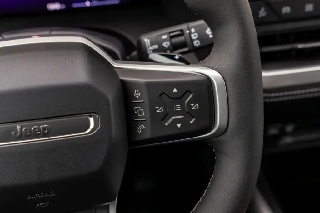 La tercera generación del Jeep Compass llega con una perspectiva global, fusionando el diseño icónico de la marca con un elevado nivel de equipamiento y una amplia dotación tecnológica pero, sobre todo, con una calidad de rodadura adaptada a los estándares europeos y, por qué no decirlo, con una puesta a punto perfecta para nuestras hoy maltrechas carreteras. Lo primero que llama la atención es que este Jeep Compass –que hemos probado en su versión eléctrica de lanzamiento– es claramente más grande que su predecesor y muestra un aspecto rotundo y cúbico que ha obligado a trabajar cada centímetro cuadrado de la carrocería para lograr un coeficiente aerodinámico de 0,29, meritorio para unos volúmenes tan poliédricos. El Jeep Compass se desmarca de sus “mellizos” de Stellantis Con 4,55 metros de longitud, Jeep lo define como SUV del segmento C, aunque sus dimensiones lo acercan claramente al segmento superior. Basado en la plataforma modular STLA Medium de Stellantis –compartida con los Peugeot 3008 y 5008, el Opel Grandland y el Citroën C5 Aircross–, el Jeep Compass se beneficia de un desarrollo de suspensiones específico orientado a lograr 20 centímetros de altura libre al suelo, con una reducción del 15 % en la aceleración vertical y un 20 % menos de balanceo de carrocería respecto a la generación anterior. El resultado sobre el asfalto es el de un buen SUV: no especialmente ágil, como corresponde a su masa y a su centro de gravedad elevado, pero sí notablemente mejor que el anterior Jeep Compass. Se inclina moderadamente en los apoyos fuertes y en las frenadas enérgicas, pero sin el efecto rebote de las suspensiones que caracterizaba a la generación precedente, poniendo en valor el trabajo de unos amortiguadores perfectamente capaces de cumplir con su trabajo. Las suspensiones están, así, bien adaptadas para recorrer caminos a buen ritmo: absorben con solvencia las irregularidades del terreno y muestran una parte final del recorrido más firme para evitar topes si se aborda una zona abrupta a más velocidad de la debida. En los caminos moderadamente rotos, el Compass pone en valor sus amplios recorridos de suspensión y la amabilidad con la que trata a sus ocupantes, y en autopista cumple con eficacia. En unos tiempos en los que nuestras carreteras acumulan socavones y baches por la falta de mantenimiento y el paso de las últimas borrascas, un vehículo como este Jeep Compass resulta más interesante de lo que parece. La dirección, además, ofrece un tacto suave, muy asistido, que minimizará el efecto “latigazo” ante un bache imprevisto, y el radio de giro es razonable para la batalla del vehículo. Al volante del Jeep Compass eléctrico, el motor de 213 CV ofrece la respuesta inmediata que cabe esperar de esta tecnología, pero con una progresión suave y lineal que casa bien con el carácter del vehículo. La frenada regenerativa está bien integrada, y el modo One Pedal –que detiene el vehículo por completo– es muy práctico, aunque resulta algo llamativo que se active mediante un botón dedicado en lugar de mediante las levas, como los otros tres niveles de regeneración. En cuanto a la autonomía homologada de 500 km WLTP, conviene aplicar el habitual factor corrector del 0,7 para hacerse una idea realista del alcance en uso cotidiano. Salto de calidad a bordo del nuevo Jeep Compass Por calidad de acabados y espacio, el habitáculo no tiene nada que ver con lo visto hasta ahora en el Jeep Compass. El puesto de conducción es cómodo, con una postura elevada muy Jeep, y las plazas traseras son amplias y adecuadas para el uso diario. El maletero ofrece 550 litros –45 más que en el anterior Jeep Compass–, ampliables con el gran hueco bajo el piso desmontable, aunque no hay maletero delantero. Un detalle relevante: el selector del cambio es un mando giratorio físico e intuitivo, en lugar del habitual conmutador lineal del resto de modelos de Stellantis, uno de los muchos detalles que indican que en Jeep se han tomado muy en serio este desarrollo y no han ido simplemente a “recarrozar” lo ya existente. El sistema Selec-Terrain ofrece cinco modos –Automático, Deportivo, Nieve, Arena/Barro y Eléctrico–, y hemos comprobado que el modo Arena permite un cierto patinamiento de las ruedas, lo que denota una buena calibración del control de tracción para ese tipo de terreno, incluso en un vehículo de tracción delantera. La insonorización es notable, por encima de la media de su segmento. La gama de lanzamiento incluye dos acabados: Altitude y First Edition. No es, con ninguno de ellos, un SUV que pretenda competir en precio, pero puede ser la opción adecuada para quienes necesiten capacidades fuera del asfalto superiores a las habituales en un 4x2. Quienes precisen un 4x4 real deberán esperar a la versión eléctrica bimotor, pero para las bacheadas carreteras de las que disfrutamos estos días, esta versión es más que suficiente. El Jeep Compass milita en el segmento más poblado del mercado, por lo que su fabricante ha decidido no competir en precio, sino ofrecer un producto que destaque por habitabilidad y bastidor. Su versión eléctrica añade economía de uso y etiqueta Cero. Así que estamos ante un modelo con argumentos para hacerlo bien, si bien su precio limitará su difusión.