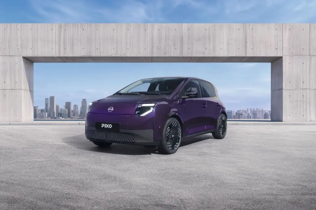Nissan presenta el nuevo PIXO, su eléctrico urbano de acceso 5 Motor16 Three-quarter front view of a purple Nissan PIXO electric city car parked beneath a modern concrete structure, with a city skyline in the background.